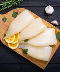 a portion of squid tubes laid on a wooden platter garnished with lemon rosemary parsley and garlic atop a black wooden table