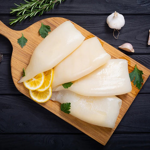 a portion of squid tubes laid on a wooden platter garnished with lemon rosemary parsley and garlic atop a black wooden table